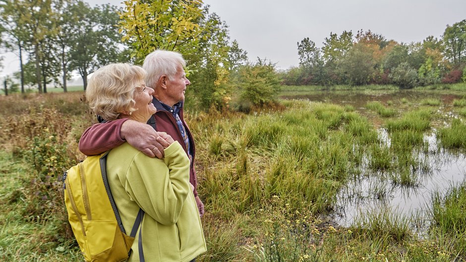 ©Florian Trykowski Älteres Paar genießt Arm in Arm den Blick auf einen Teich.