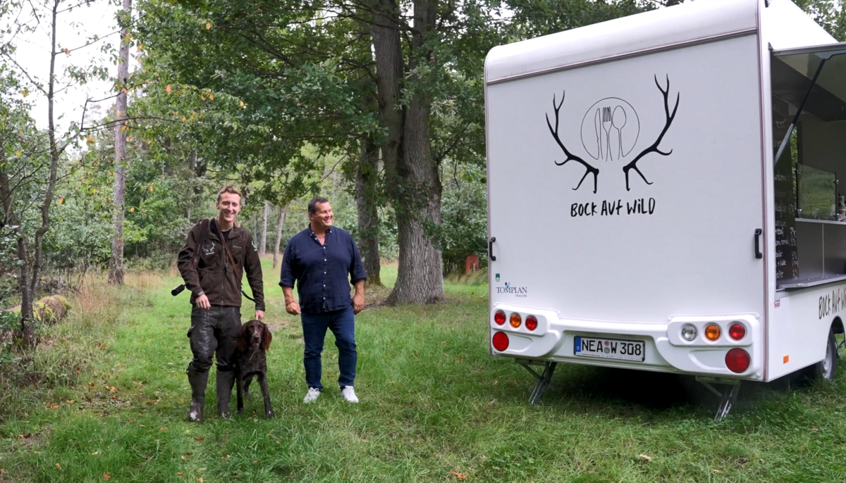 Zwei Männer mit einem Hund im Wald neben einem Foodtruck