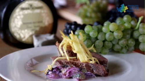 Entenbrust mit Traubengemüse und Kartoffelstroh, im Hintergrund ein Bocksbeutel und Trauben