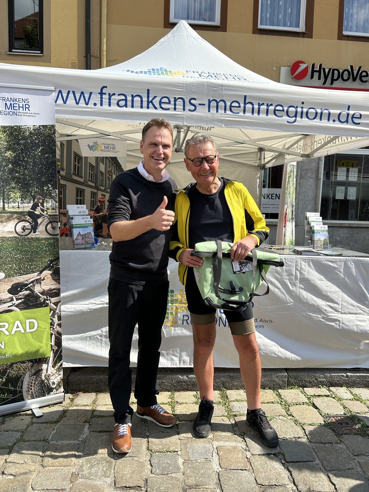 Zwei Personen, einer davon in Fahrradkleidung mit Fahrradtasche in den Händen
