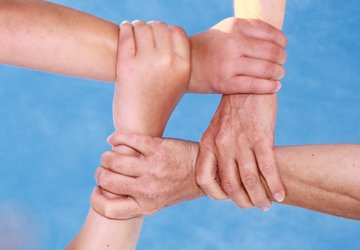 Vier Hände fassen sich jeweils am Handgelenk des Nächsten, sodass eine Art Raute entsteht