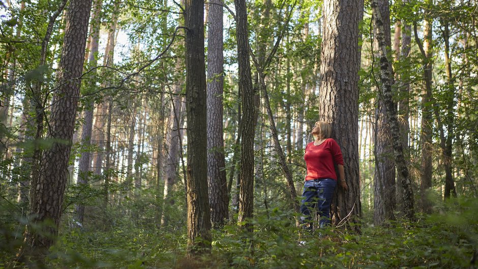©Ines Männl Eine Frau lehnt im Wald an einem Baum.
