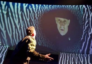 Bild aus einem Theaterstück mit einem Mann und einer Videoprojektion.