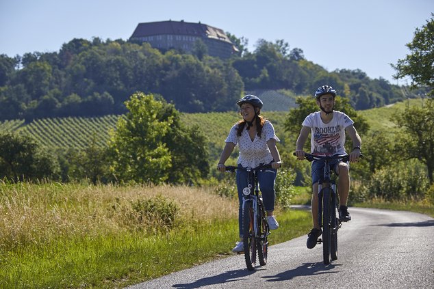 Zwei Radfahrer fahren auf einem Feldweg vor der Kulisse der Burg Hoheneck