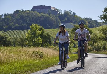 Zwei Radfahrer fahren auf einem Feldweg vor der Kulisse der Burg Hoheneck